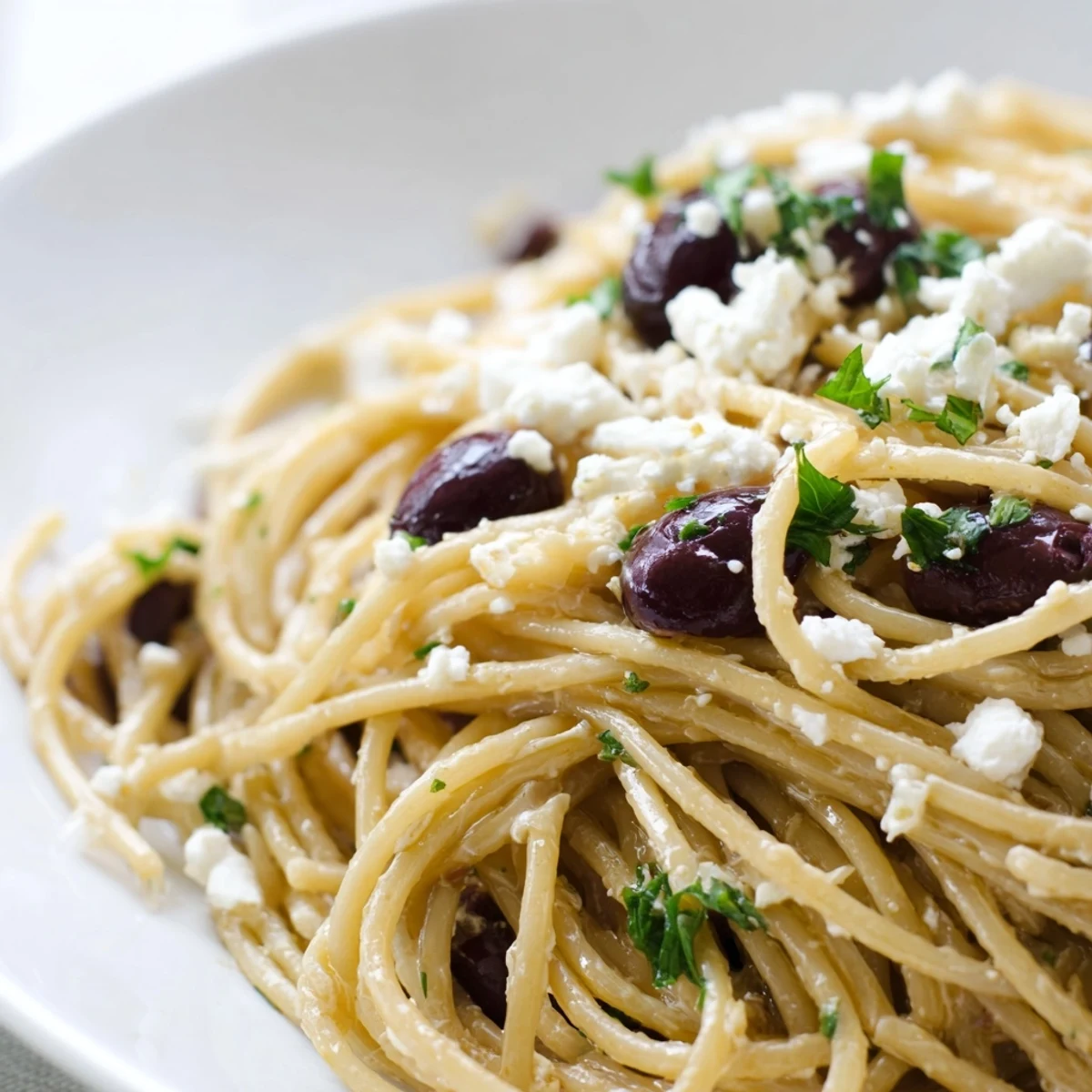In a shallow bowl, Greek Chicken Spaghetti features juicy grilled chicken slices, briny Kalamata olives, and crumbled feta over tangled pasta.