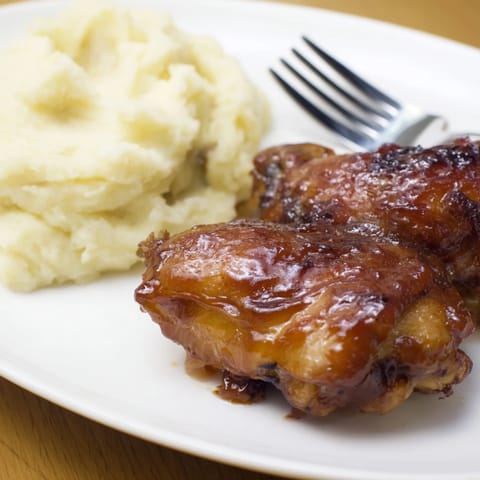 Oven-baked chicken thighs dripping in honey BBQ sauce next to creamy mashed potatoes.  
