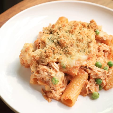 A close-up shot of creamy tuna pasta bake, savory and filled with visible peas and tomatoes.