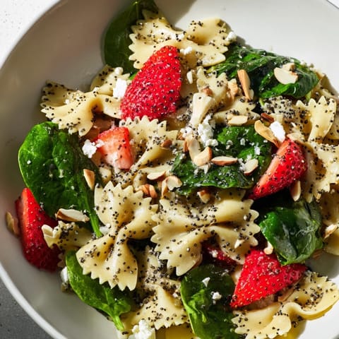 A close-up of Spring Spinach Strawberry Pasta Salad with crumbled feta, toasted almonds, and fresh basil leaves on a serving platter.