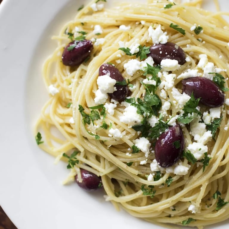 A generous serving of Greek Chicken Spaghetti on a dinner plate, garnished with feta and olives, ready to enjoy.